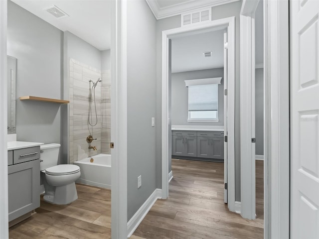 full bathroom with hardwood / wood-style flooring, tiled shower / bath combo, crown molding, vanity, and toilet