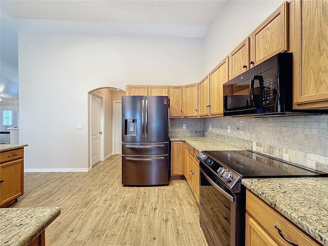 kitchen with light stone countertops, light hardwood / wood-style flooring, tasteful backsplash, and black appliances