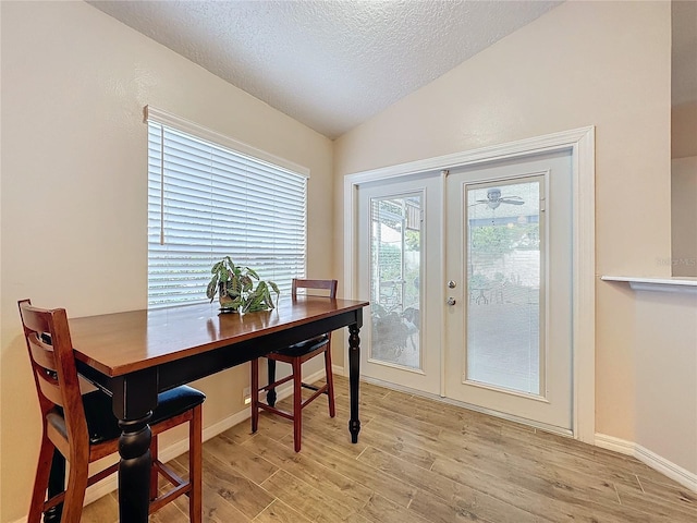 dining area featuring light hardwood / wood-style flooring, lofted ceiling, a textured ceiling, and french doors