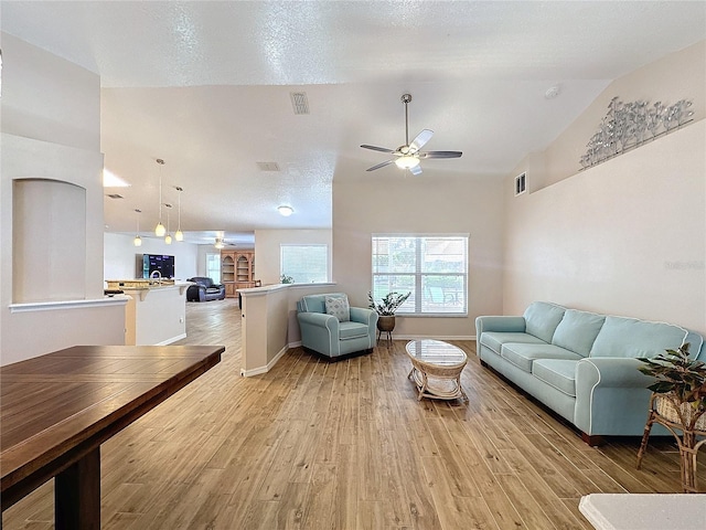 living room featuring light wood-type flooring, a textured ceiling, lofted ceiling, and ceiling fan