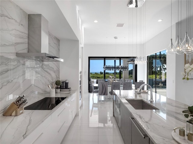 kitchen with light stone countertops, wall chimney exhaust hood, hanging light fixtures, and a healthy amount of sunlight