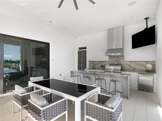 kitchen with stainless steel fridge, tasteful backsplash, wall chimney exhaust hood, light tile patterned floors, and ceiling fan