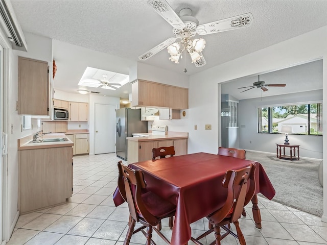 tiled dining area featuring a textured ceiling, ceiling fan, a skylight, and sink