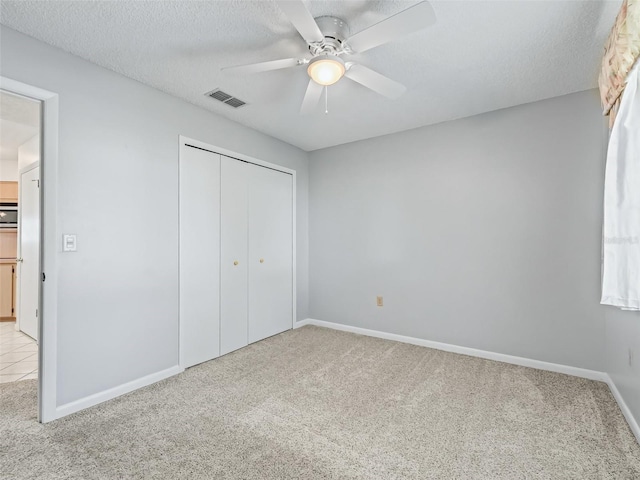 unfurnished bedroom with a textured ceiling, ceiling fan, light colored carpet, and a closet