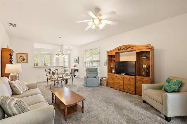 living room featuring ceiling fan with notable chandelier, carpet flooring, and plenty of natural light