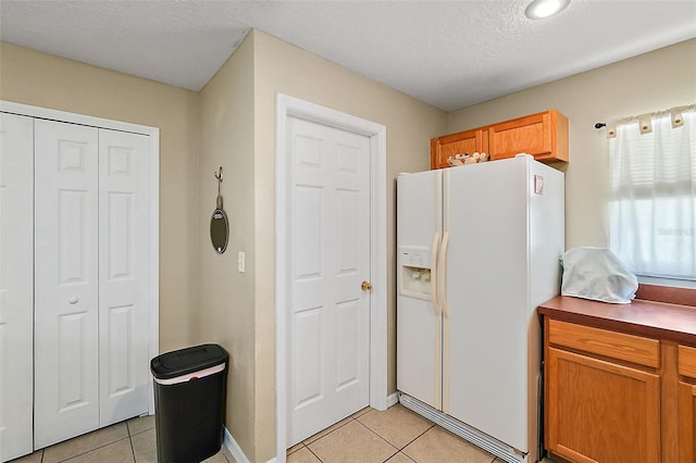 kitchen with a textured ceiling, light tile patterned floors, and white refrigerator with ice dispenser