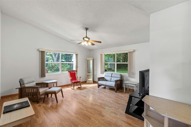 living area featuring ceiling fan, light wood-type flooring, plenty of natural light, and vaulted ceiling