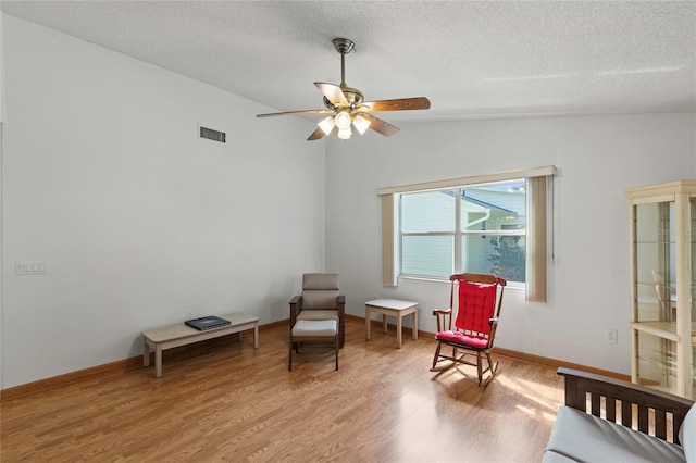 sitting room with ceiling fan, a textured ceiling, light wood-type flooring, and vaulted ceiling