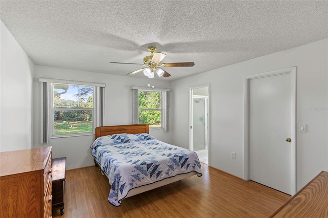 bedroom featuring light hardwood / wood-style flooring, ceiling fan, ensuite bathroom, and a textured ceiling