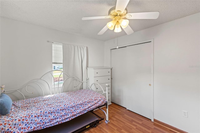 bedroom with light wood-type flooring, a textured ceiling, ceiling fan, and a closet