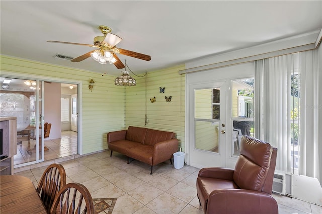 living room with ceiling fan, wooden walls, and light tile patterned floors