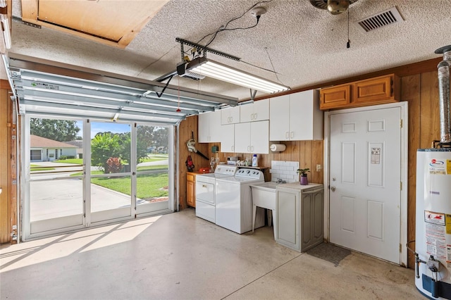 garage featuring gas water heater, wooden walls, sink, and independent washer and dryer