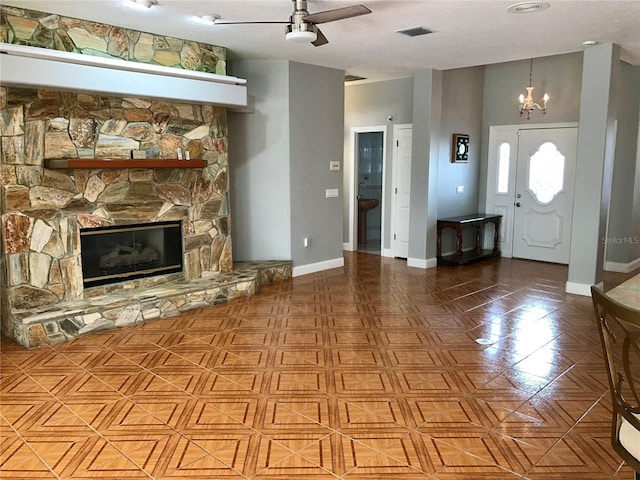 unfurnished living room featuring ceiling fan with notable chandelier and a stone fireplace