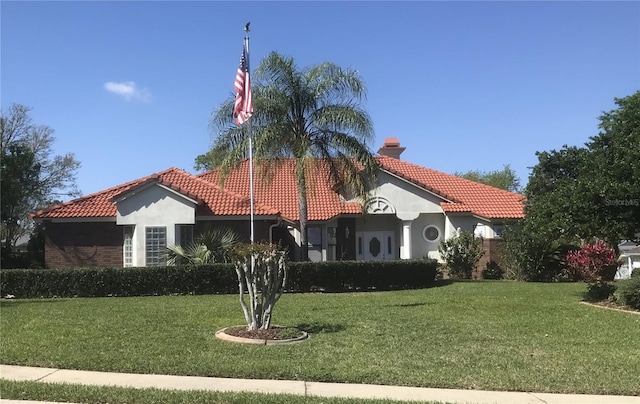 view of front of property with a tile roof, stucco siding, a front lawn, and a chimney