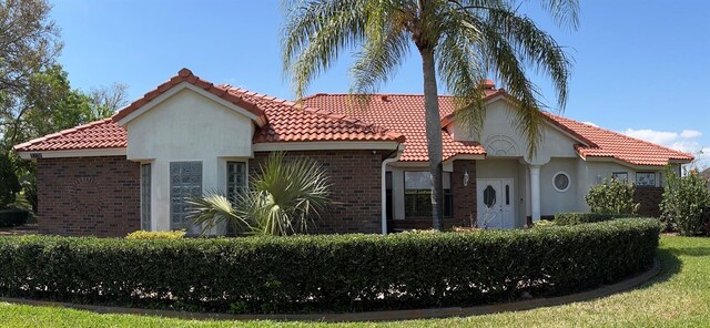 view of front facade with stucco siding, brick siding, and a tile roof