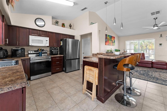 kitchen featuring appliances with stainless steel finishes, high vaulted ceiling, a breakfast bar area, light tile patterned floors, and ceiling fan