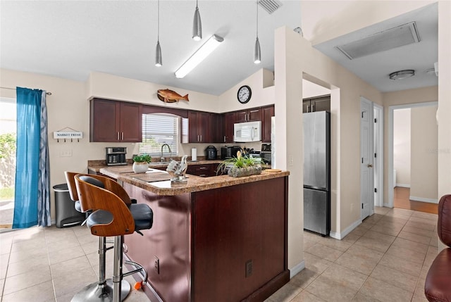 kitchen featuring lofted ceiling, hanging light fixtures, light tile patterned flooring, and stainless steel fridge