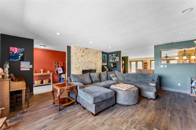 living room featuring wood-type flooring, a textured ceiling, and a stone fireplace