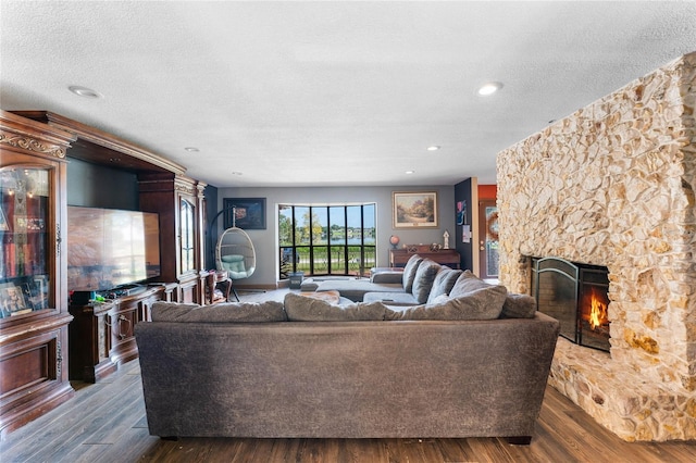 living room featuring a textured ceiling, a stone fireplace, and dark hardwood / wood-style floors