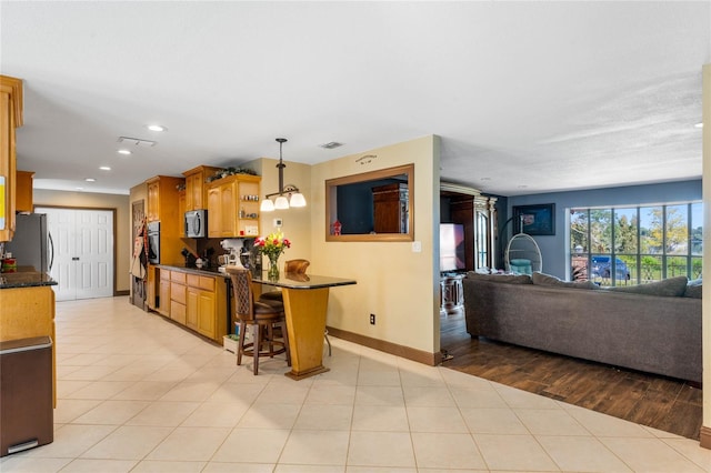 kitchen featuring a breakfast bar, appliances with stainless steel finishes, light wood-type flooring, and decorative light fixtures