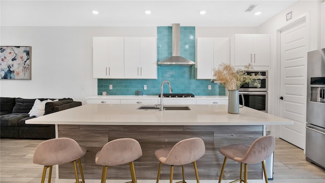 kitchen with a kitchen breakfast bar, a kitchen island with sink, wall chimney exhaust hood, and light wood-type flooring