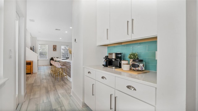 bar featuring tasteful backsplash, light hardwood / wood-style flooring, and white cabinets