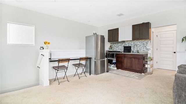 kitchen with dark brown cabinets, sink, stainless steel refrigerator, decorative backsplash, and light carpet