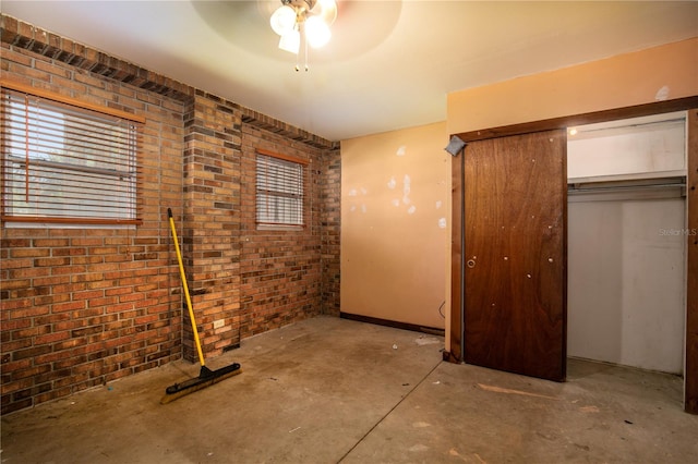 unfurnished bedroom with ceiling fan, a closet, and brick wall