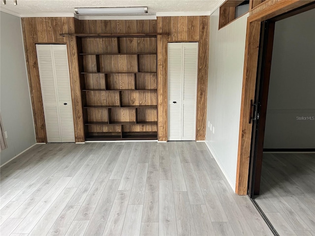 interior space featuring wooden walls, light hardwood / wood-style floors, a closet, and crown molding