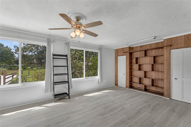 unfurnished room with a wealth of natural light, wood walls, ceiling fan, and light wood-type flooring