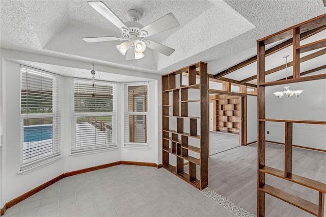 unfurnished room featuring light wood-type flooring, a textured ceiling, a tray ceiling, ceiling fan with notable chandelier, and vaulted ceiling