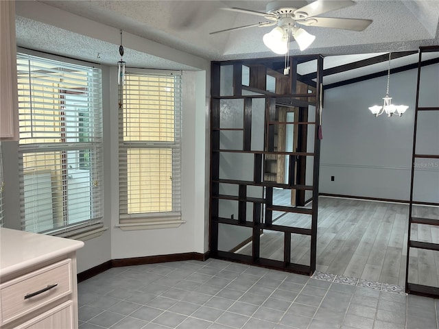 spare room featuring ceiling fan with notable chandelier, light wood-type flooring, lofted ceiling, and a textured ceiling