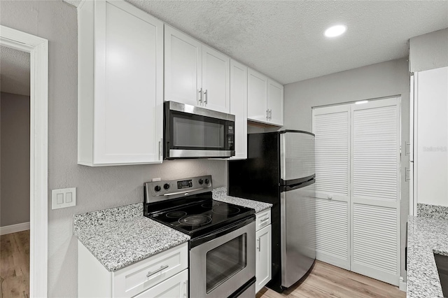 kitchen featuring stainless steel appliances, light stone countertops, white cabinets, and light hardwood / wood-style floors