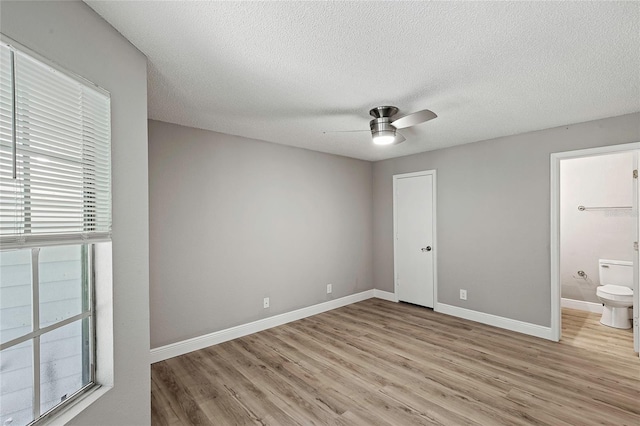 unfurnished bedroom featuring ceiling fan, ensuite bathroom, a textured ceiling, and light wood-type flooring