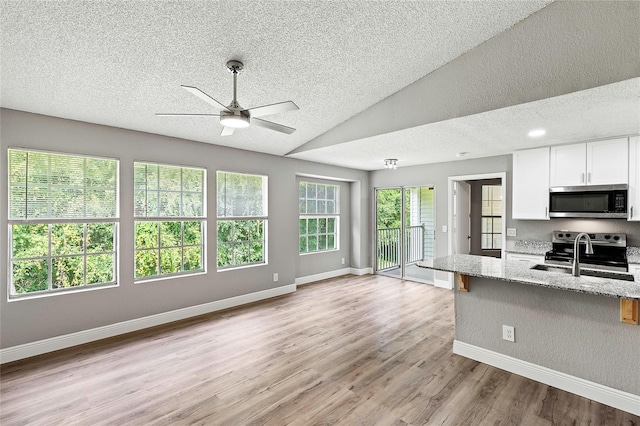 kitchen with appliances with stainless steel finishes, white cabinetry, light stone counters, light hardwood / wood-style floors, and vaulted ceiling