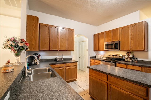 kitchen with appliances with stainless steel finishes, a textured ceiling, sink, and light tile patterned floors