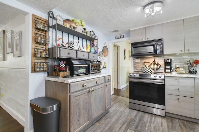 kitchen featuring light stone countertops, stainless steel range, dark wood-type flooring, backsplash, and a textured ceiling