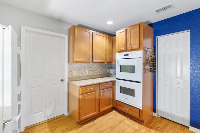 kitchen featuring white appliances, light hardwood / wood-style flooring, and tasteful backsplash