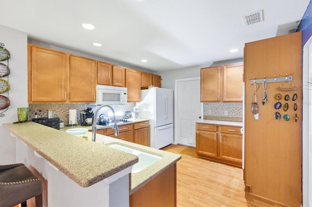 kitchen featuring light wood-type flooring, white appliances, a breakfast bar, and kitchen peninsula