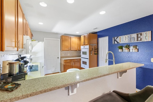 kitchen with kitchen peninsula, sink, white appliances, and a breakfast bar area