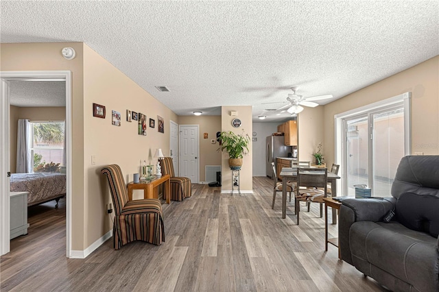 living room with light wood-type flooring, ceiling fan, and a textured ceiling