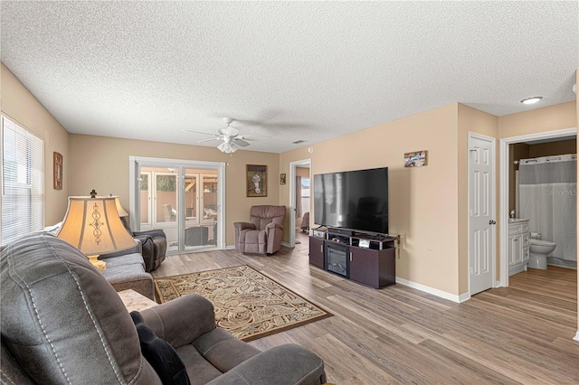 living room with light wood-type flooring, a textured ceiling, ceiling fan, and a wealth of natural light