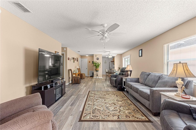 living room featuring light hardwood / wood-style flooring, a textured ceiling, and ceiling fan