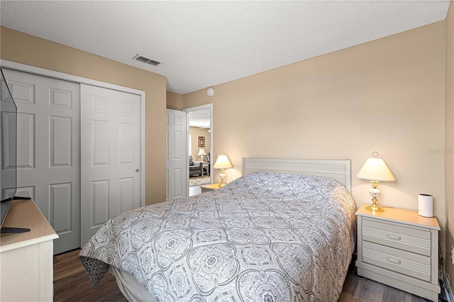 bedroom with a textured ceiling, dark wood-type flooring, and a closet