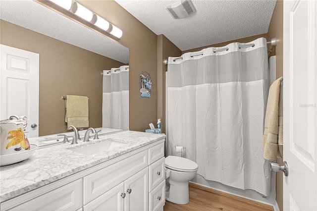 bathroom with wood-type flooring, vanity, toilet, and a textured ceiling