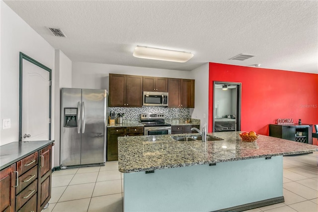 kitchen with an island with sink, stainless steel appliances, a textured ceiling, and sink