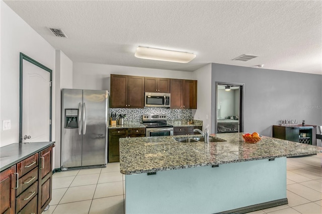 kitchen featuring an island with sink, stainless steel appliances, sink, and a textured ceiling