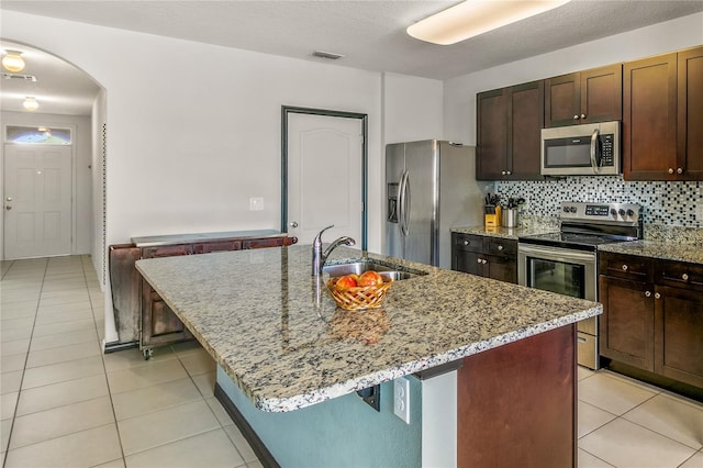 kitchen with light stone counters, sink, a kitchen island with sink, stainless steel appliances, and decorative backsplash