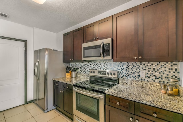 kitchen with dark brown cabinets, light stone counters, tasteful backsplash, stainless steel appliances, and light tile patterned floors