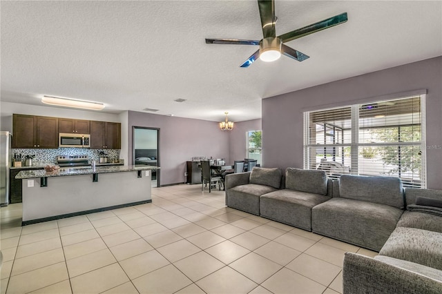 tiled living room with ceiling fan with notable chandelier and a textured ceiling